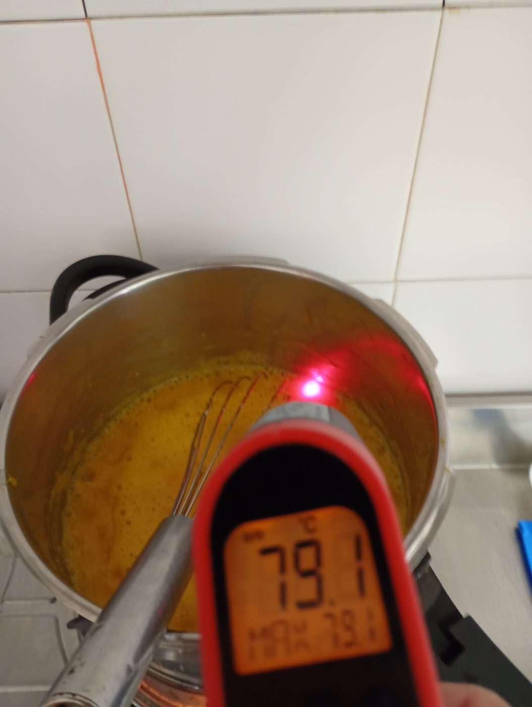 Salsa amarilla cocinándose en una olla mientras se mide la temperatura con un termómetro